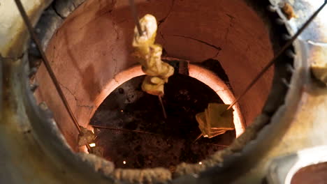 long skewer of tandoori chicken is removed from traditional tandoor oven in indian kitchen, slider close up slow motion hd