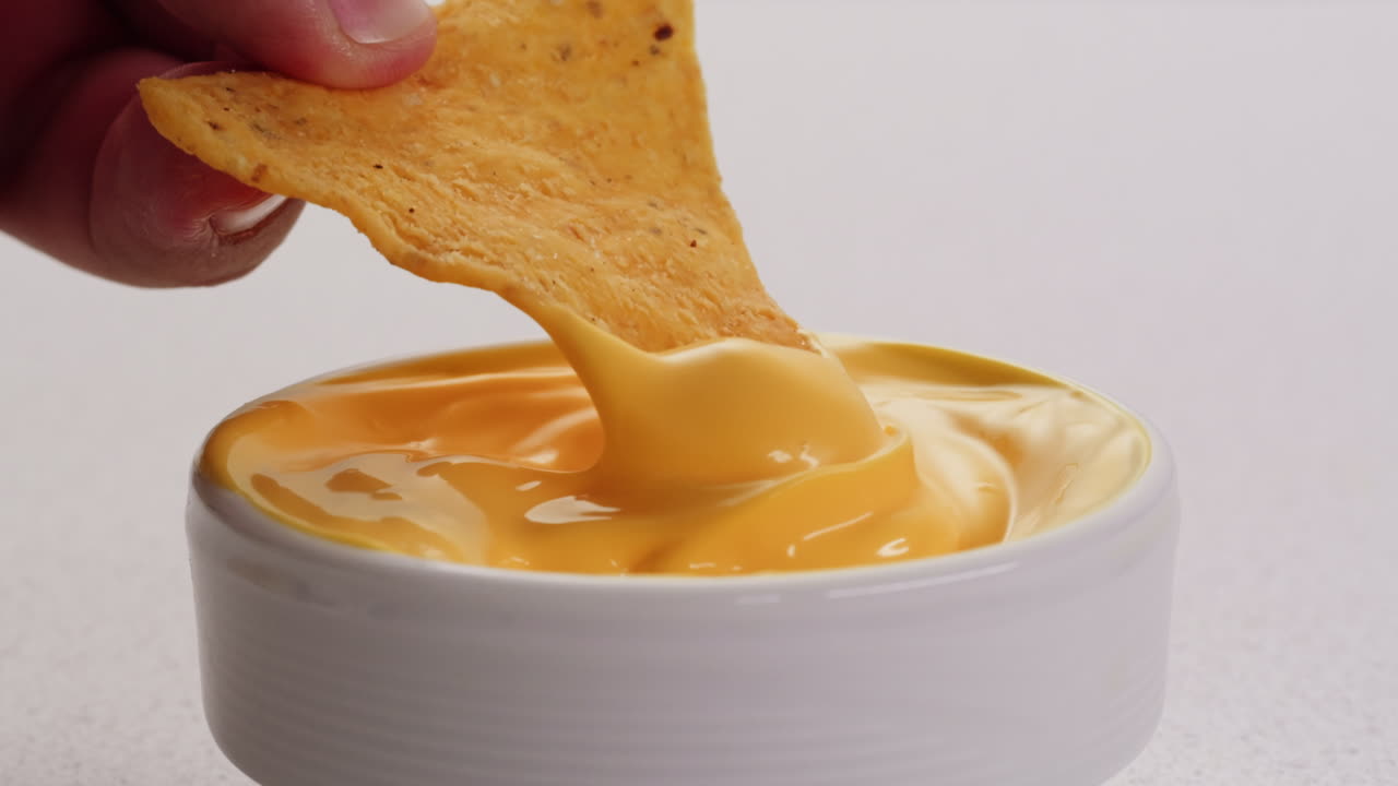 Hand dipping a tortilla chip into cheese dip
