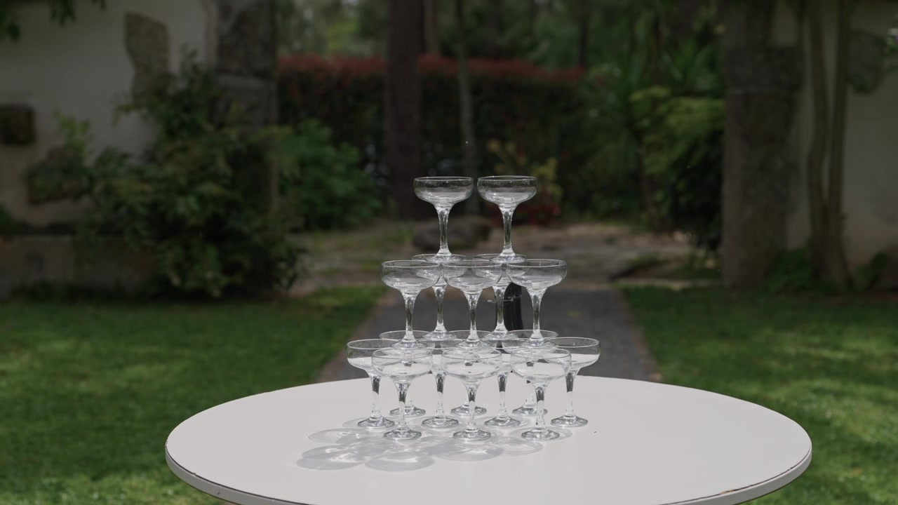 Pirâmide de taças de champanhe empilhadas em uma mesa branca em uma festa ao ar livre em um jardim verde