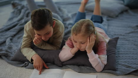 brother and sister studying with classbook at home. siblings touching book pages