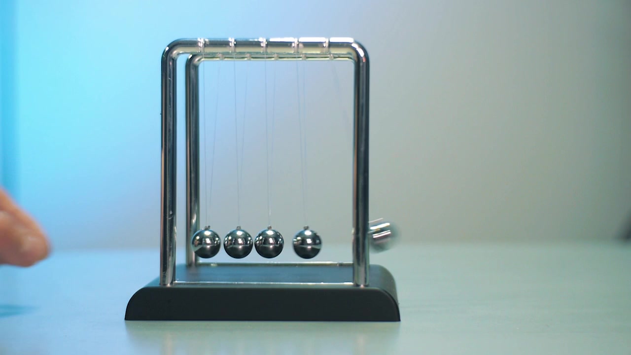 Pêndulo de Newton sobre a mesa cinza com fundo branco e azul. Bolas de metal em movimento num fio. Bolas de impacto.