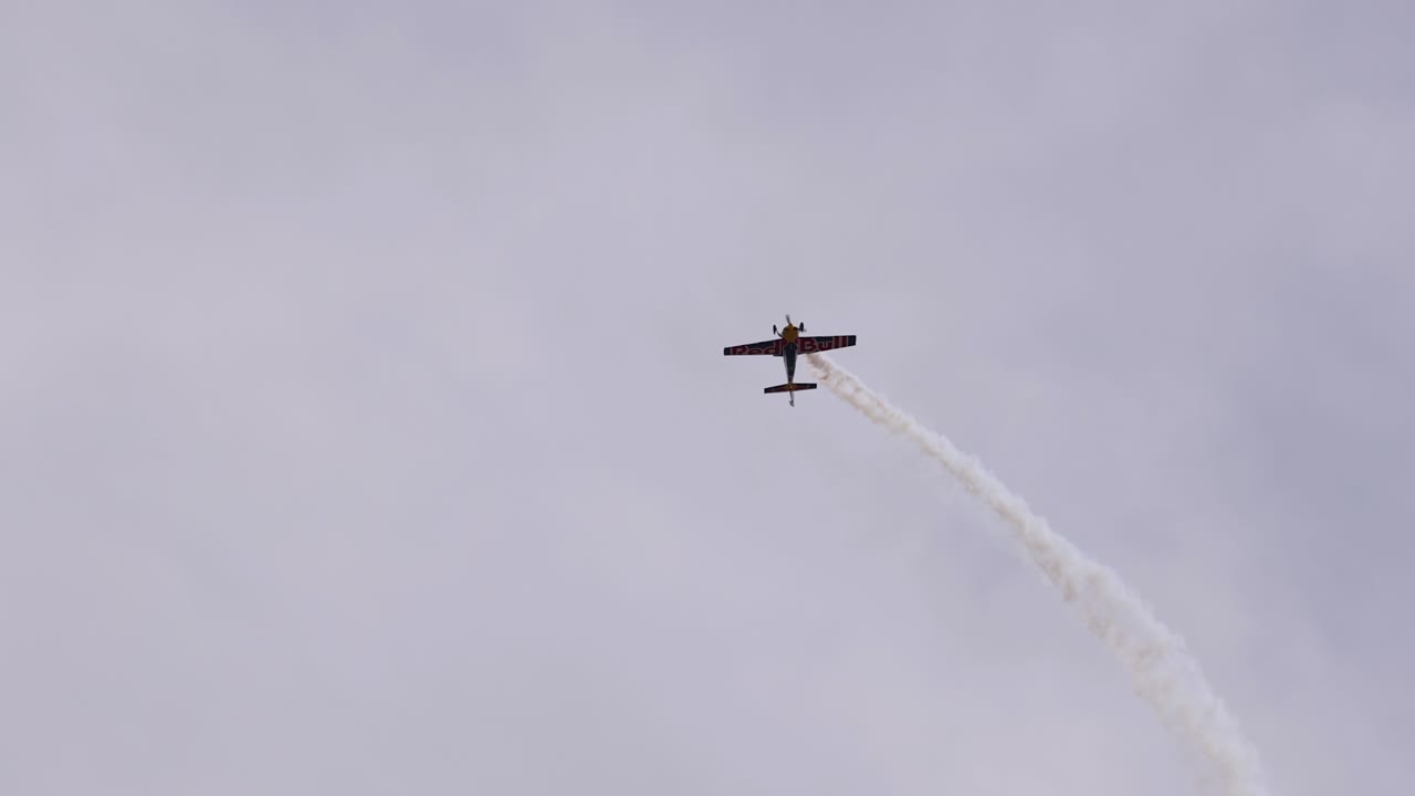 An aerobatic plane executes dynamic stunts, leaving smoke trails against a cloudy sky, showcasing precision and skill