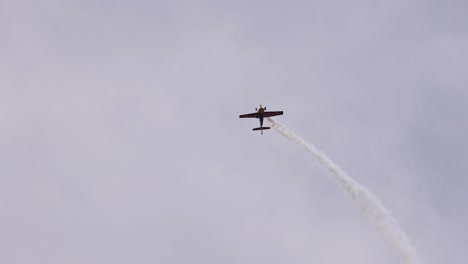 an aerobatic plane executes dynamic stunts, leaving smoke trails against a cloudy sky, showcasing precision and skill