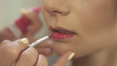 Make-up-artist-applying-red-lipstick-using-a-brush.-Close-Up-view.-Slow-Motion-shot