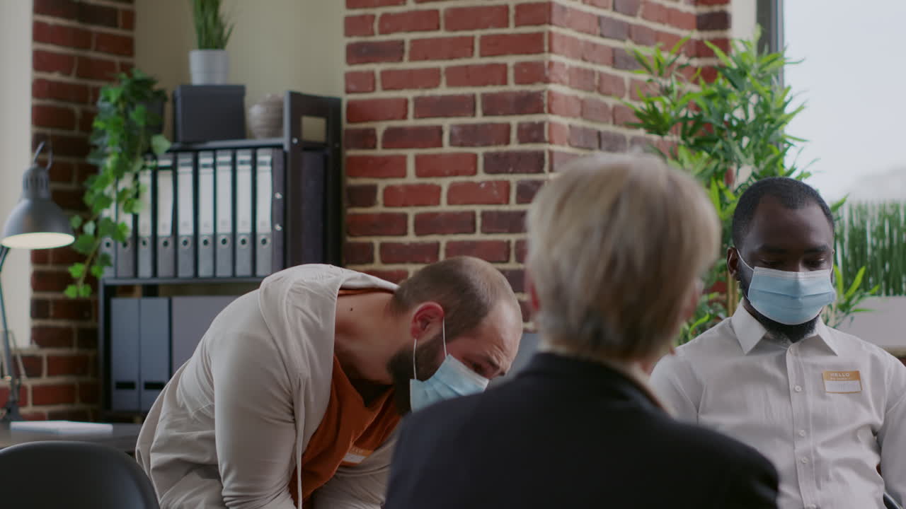 Man with face mask having desperate reaction in front of people at aa group meeting