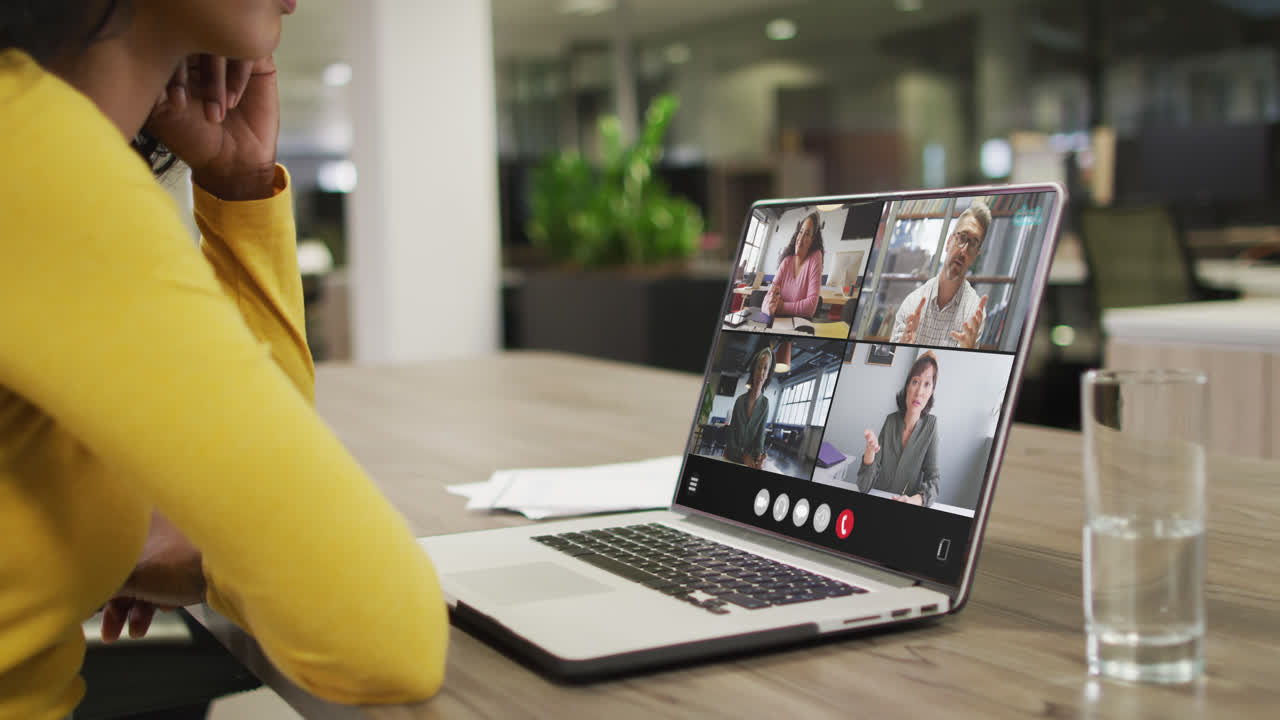 Biracial woman using laptop for video call, with diverse business colleagues on screen