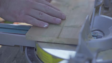 man's hands putting wooden plank on mitre saw platform to prepare for cutting in workshop