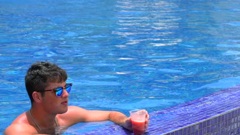 Un-Joven-Adulto-En-La-Piscina-Del-Complejo-Bebe-Una-Bebida-Daiquiri-De-Fresa-Y-Mira-El-Hermoso-Océano