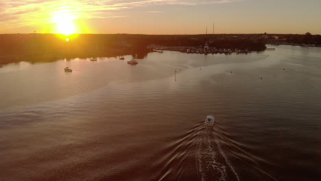 Vista-Aérea-De-Una-Lancha-Motora-Que-Ingresa-A-Un-Hermoso-Puerto-Pequeño-En-Un-Río-Tranquilo-Bajo-Una-Colorida-Puesta-De-Sol