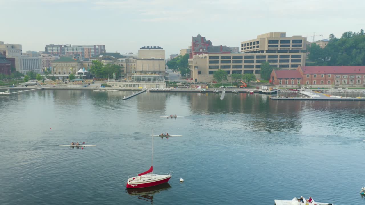 Aerial, people rowing kayaks on calm lake with city backdrop, truck right