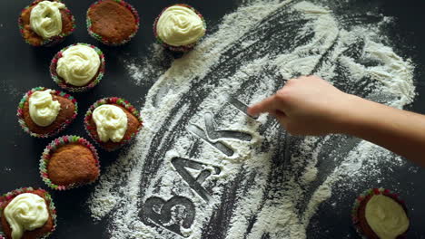 Baking-concept.-Finger-writing-word-baking-on-flour-at-kitchen-table