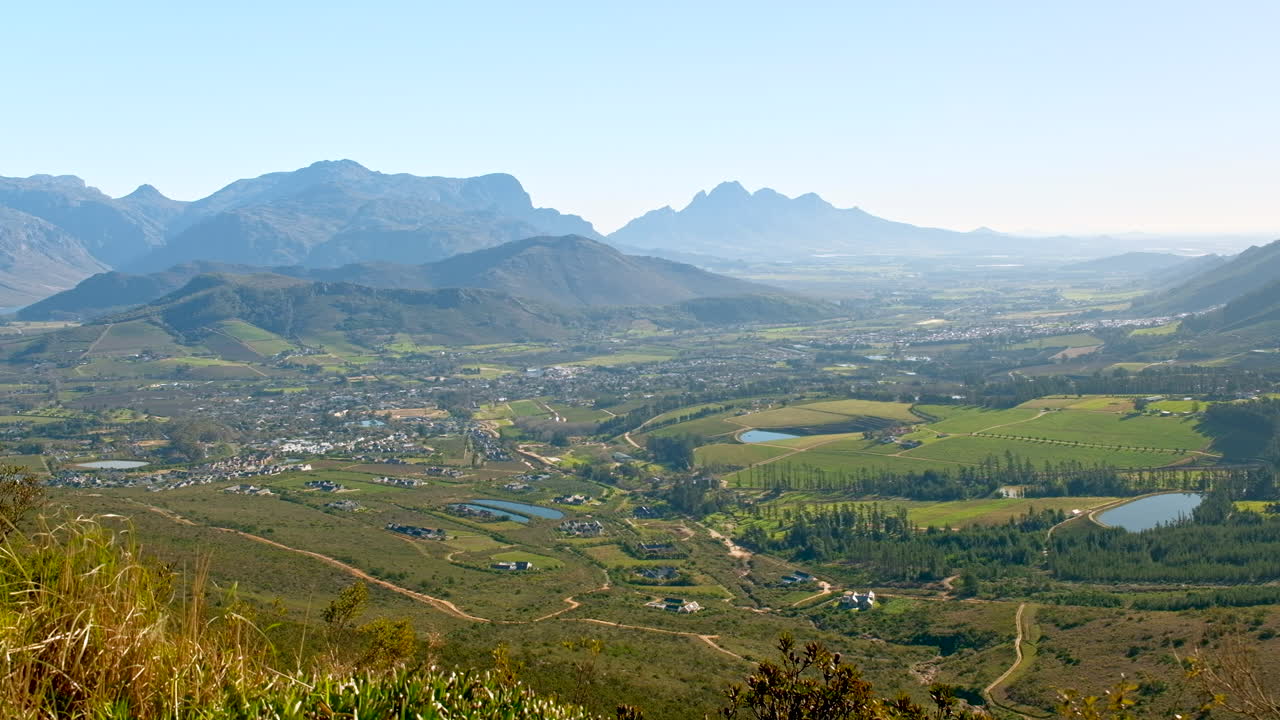 Panoramic view of a lush valley with a town, farmlands, and mountains under a clear sky
