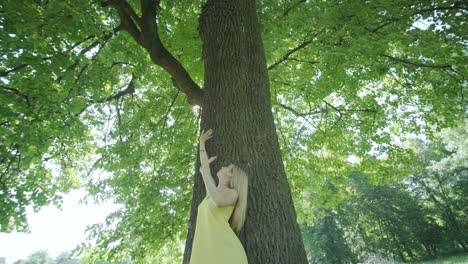 woman in yellow dress dancing by tree in summer park