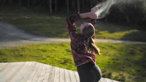 slow motion of a young woman throwing white powder on a wooden platform at golden hour sun set