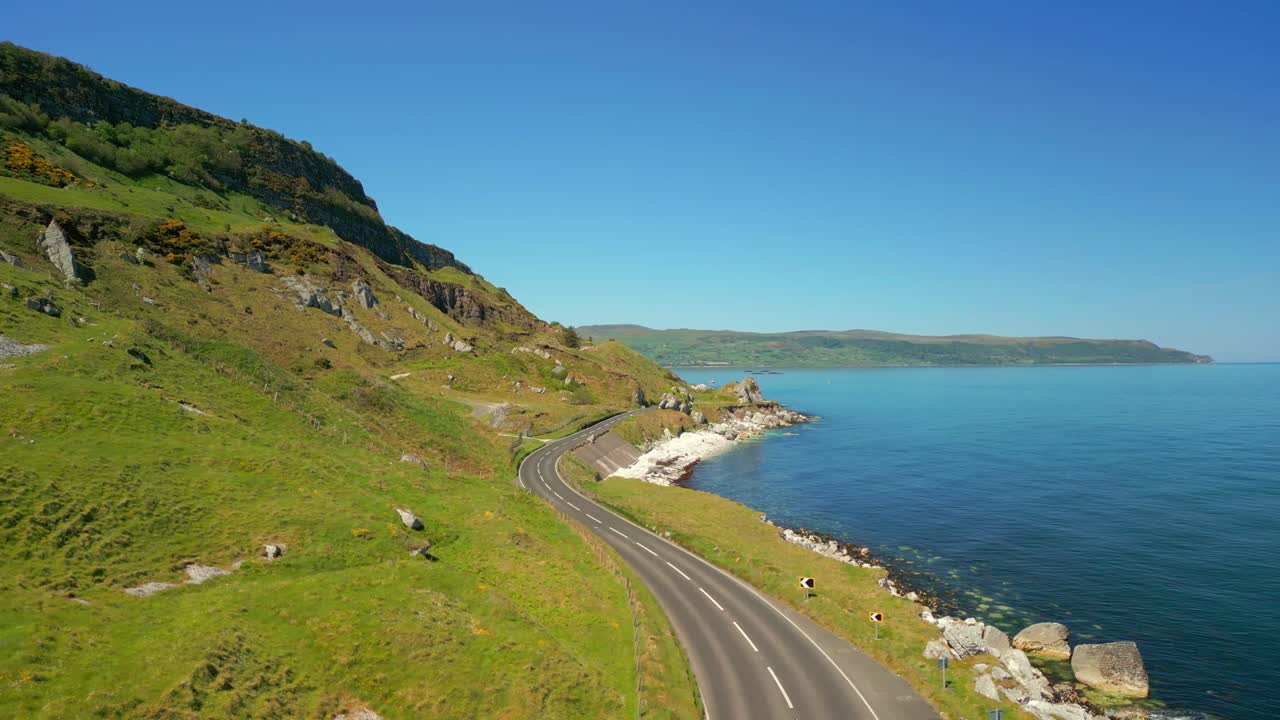 Aerial video of the Causeway Coastal Route at Glenarm in County Antrim, Northern Ireland, UK on a bright and sunny day. The camera travels over a road. Filmed in 4K, 60FPS and with Rec709 color.
