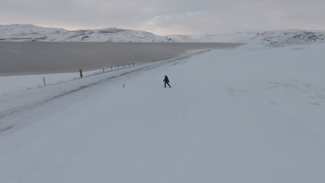 orbit view around woman crossing the snowy road in countryside, iceland