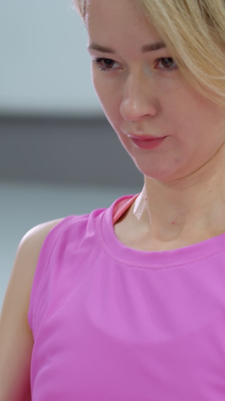 mujer con traje de entrenamiento rosa realiza ejercicios de sentada, involucrando los músculos del núcleo mientras se acuesta en una alfombra de yoga púrpura, vista parcial de las piernas de otra persona en el fondo