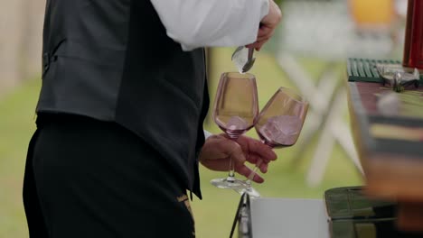 bartender adding ice cubes into two wine glasses at an outdoor event