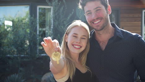 Portrait-Of-Hugging-Couple-Standing-Outdoors-In-Front-Of-House-Holding-Keys