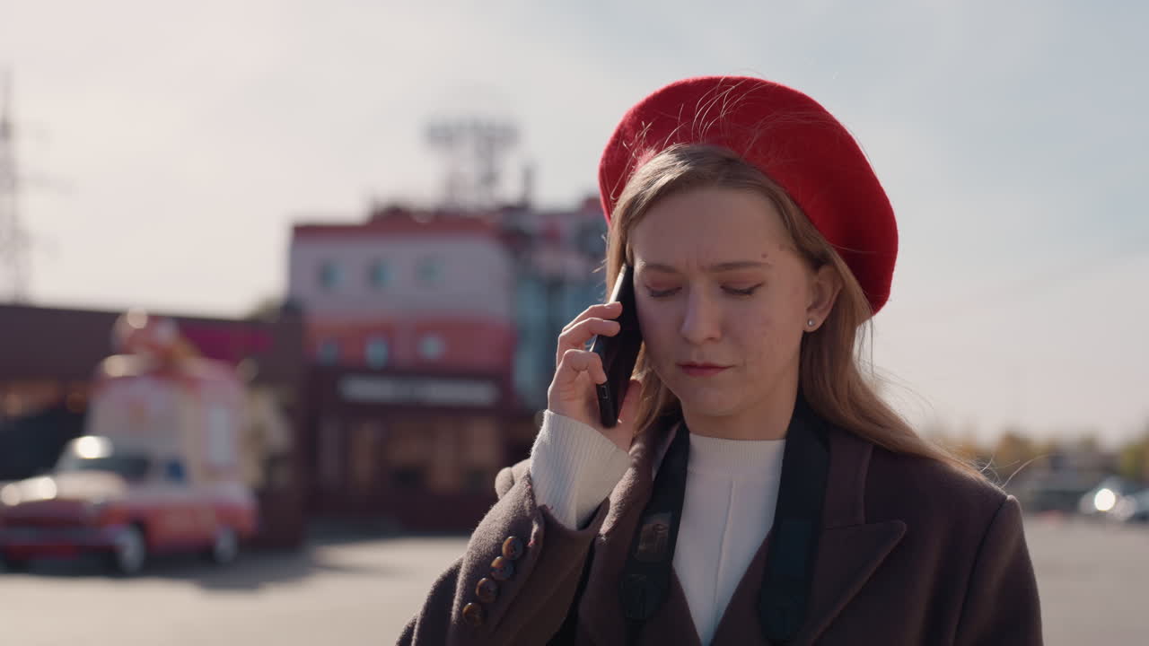 Una donna in città guarda nervosamente il telefono. Una donna ansiosa è in piedi per strada esaminando attentamente il suo telefono. Una donna nervosa in un ambiente urbano controlla il suo telefono vicino a vetrine vintage e un veicolo.