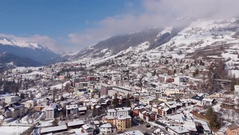 aerial establishing shot of white city in switzerland. sunny winter day in small town with colored houses and snowy roods. push out wide shot. snowy peaks of mountains in distance.quiet idyllic nature