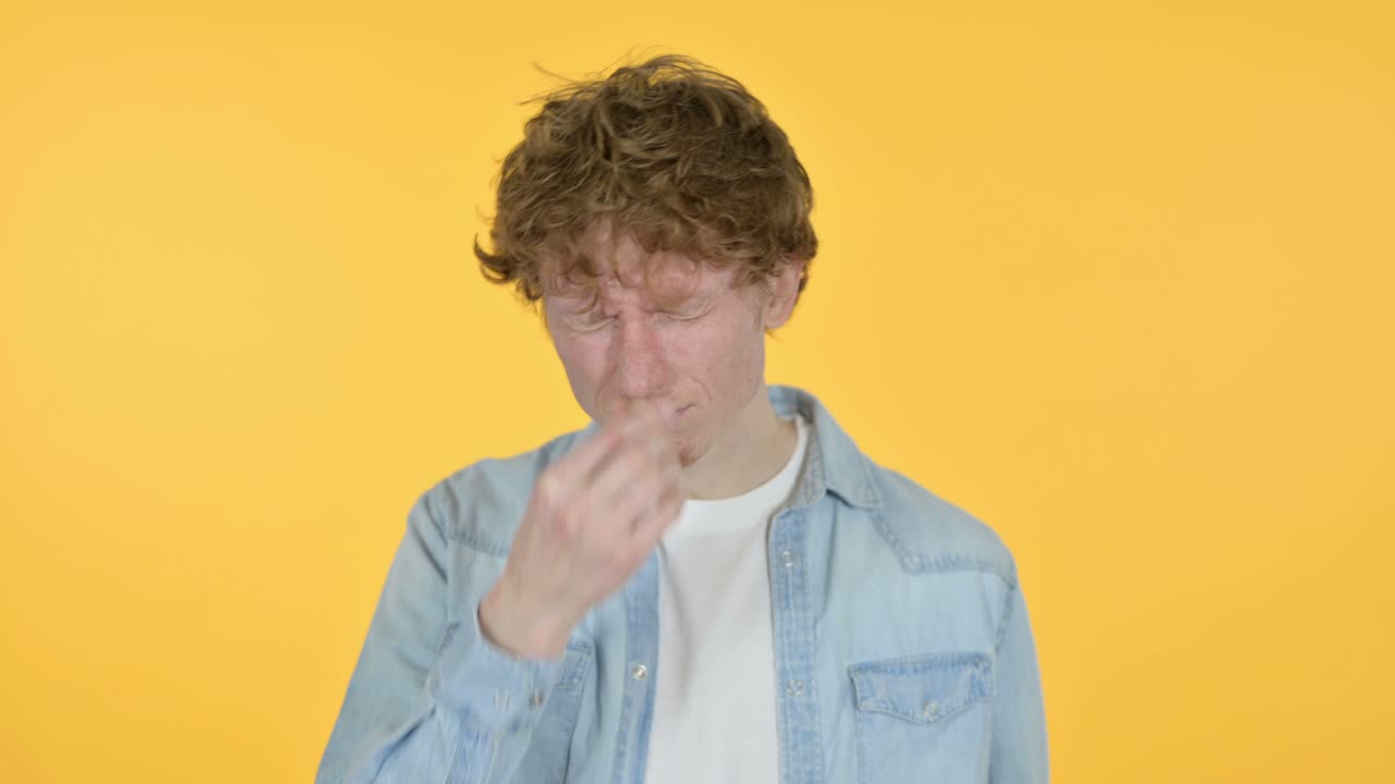 Giovane uomo dai capelli rossi con mal di testa, sfondo giallo.