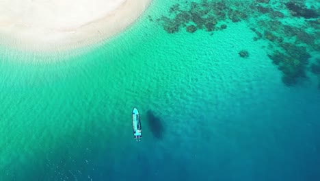 aerial top down of deep bleu indian ocean sea water with coral reef and white sand tropical beach , drone fly above small sailboat