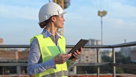 Kaukasische-Junge-Schöne-Architektin-Oder-Bauarbeiterin-Mit-Bauarbeiterhelm,-Die-Auf-Dem-Dach-Der-Baustelle-Steht-Und-Ein-Tablet-Gerät-Verwendet,-Tippt-Und-Scrollt.