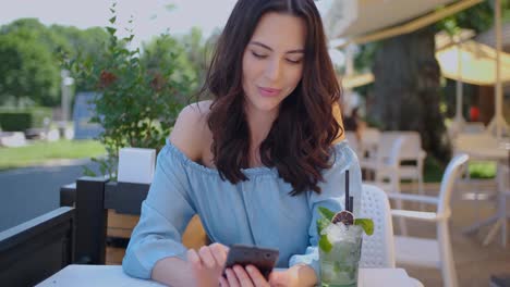 Pretty-brunette-woman-sitting-in-outdoor-restaurant-and-using-her-mobile-phone