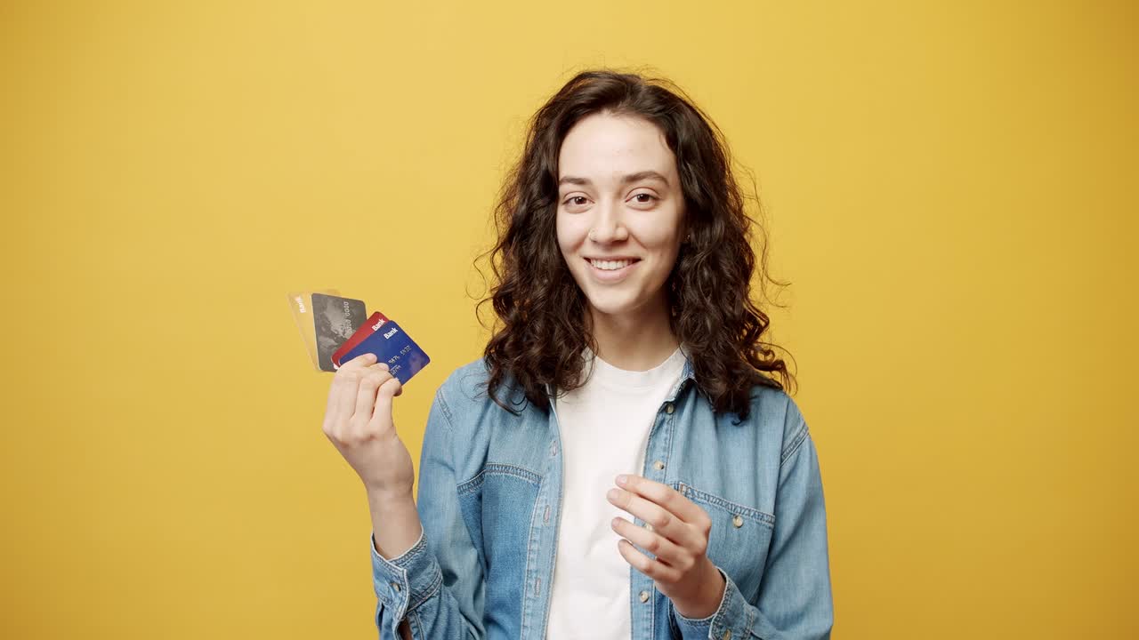 una chica feliz y sonriente posando con una tarjeta de crédito en la mano, filmada en el estudio.