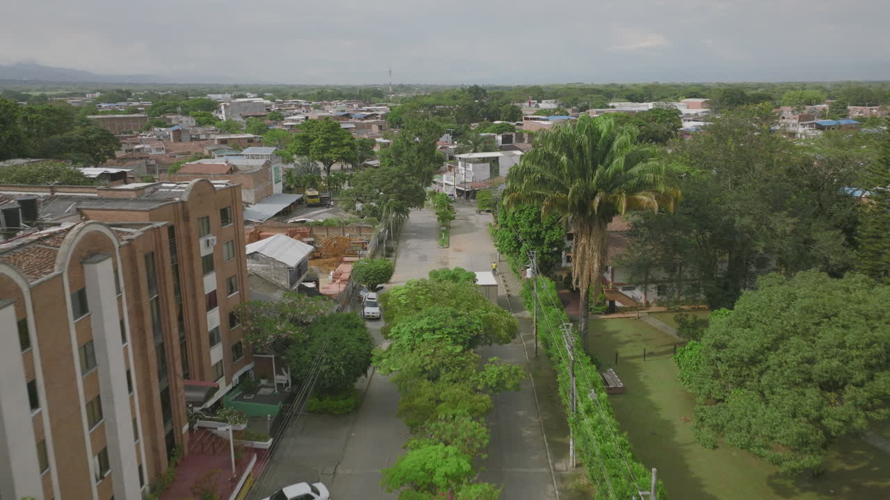 Filmagem aérea acompanhando um caminhão baú descendo uma rua arborizada em Jamundí, Colômbia