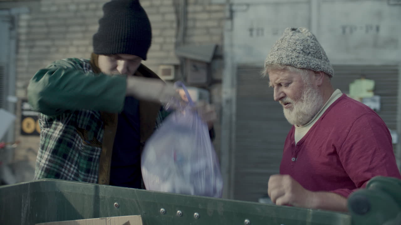 Two Homeless Men Searching through Garbage Bin Together in Backstreet
