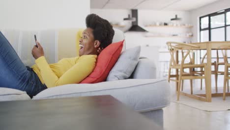 feliz mujer afroamericana acostada en el sofá usando un teléfono inteligente