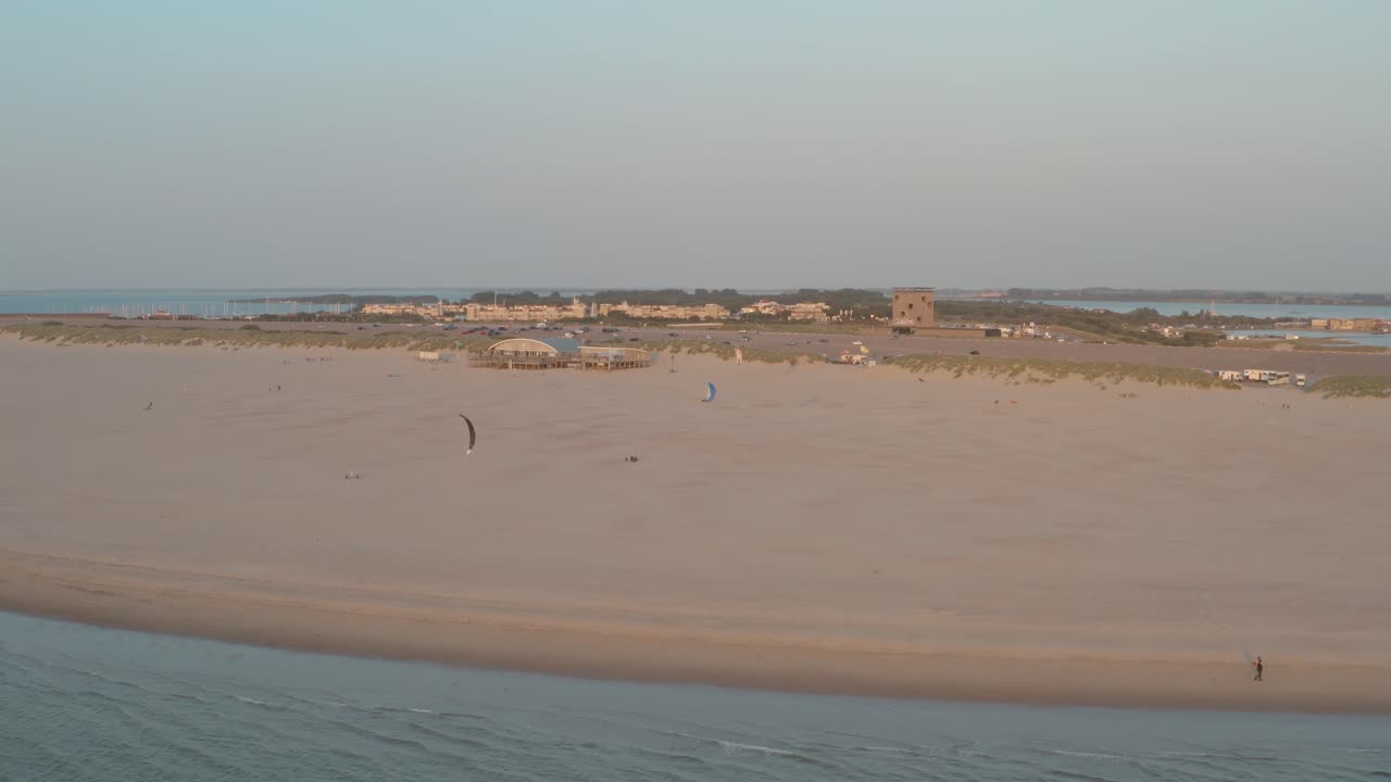 drone cinemático - panorama aéreo que rodea la playa de naturaleza verde y arenosa al atardecer con turistas y personas con buggykiting en zelanda en el mar del norte, países bajos, 30p