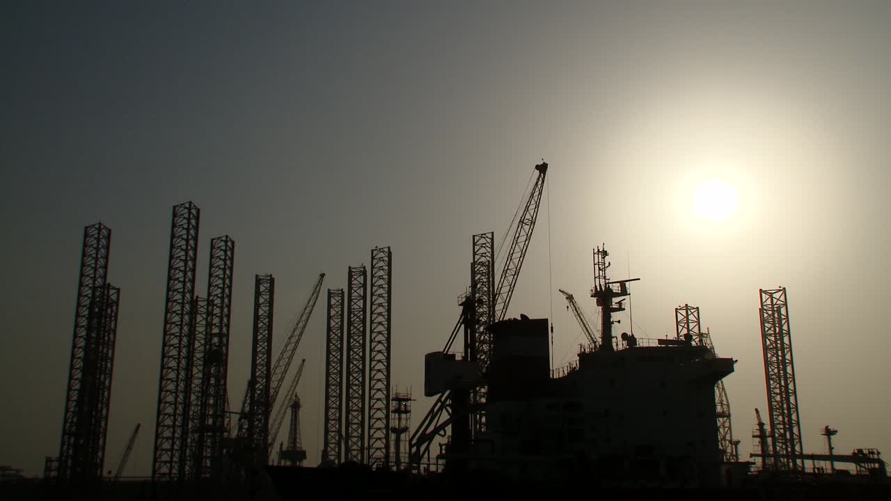 Panorering ned på silhuet af olieboreplatforme i havn, der afventer reparationer og vedligeholdelse på tørdokken i Bahrain