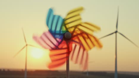 pinwheel rotate color plastic, windmill with blowing wind against  of wind turbines wind park sunset sky of sunny day summer. descending bright disk of sun beyond horizon on field. lens flare. relax