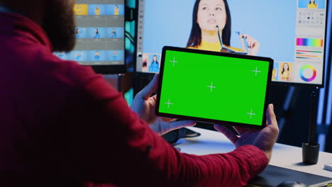 el editor de fotos usa una tableta de pantalla verde para ver podcasts en línea mientras mira imágenes