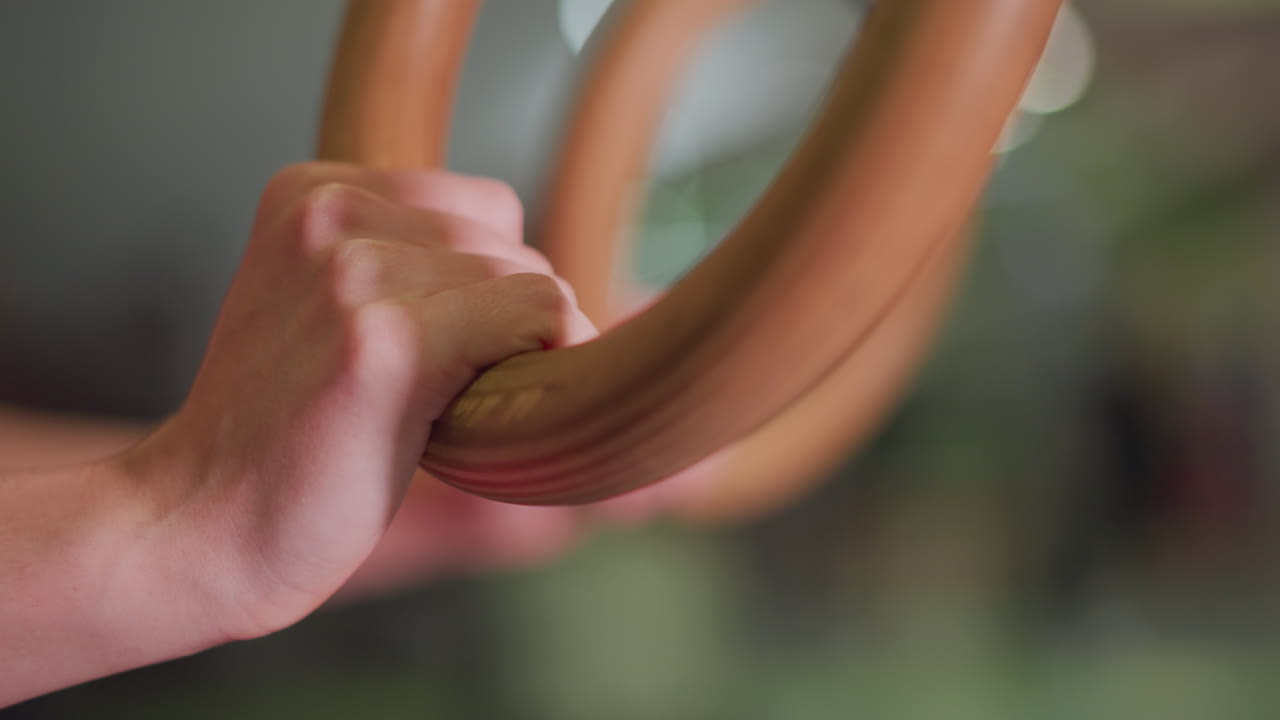 closeup hands gripping wooden ring, steady tension and wrist engagement, shallow depth of field with gym bokeh, training warmup focusing on grip strength and control, coach demonstration vibe