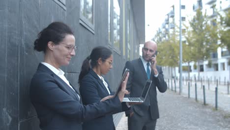 side view of business team standing at office building, using tablet, laptop and phone