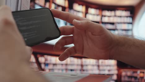 close-up of a hand using a smartphone with ai content on screen, set in a library environment—showing modern digital learning and research