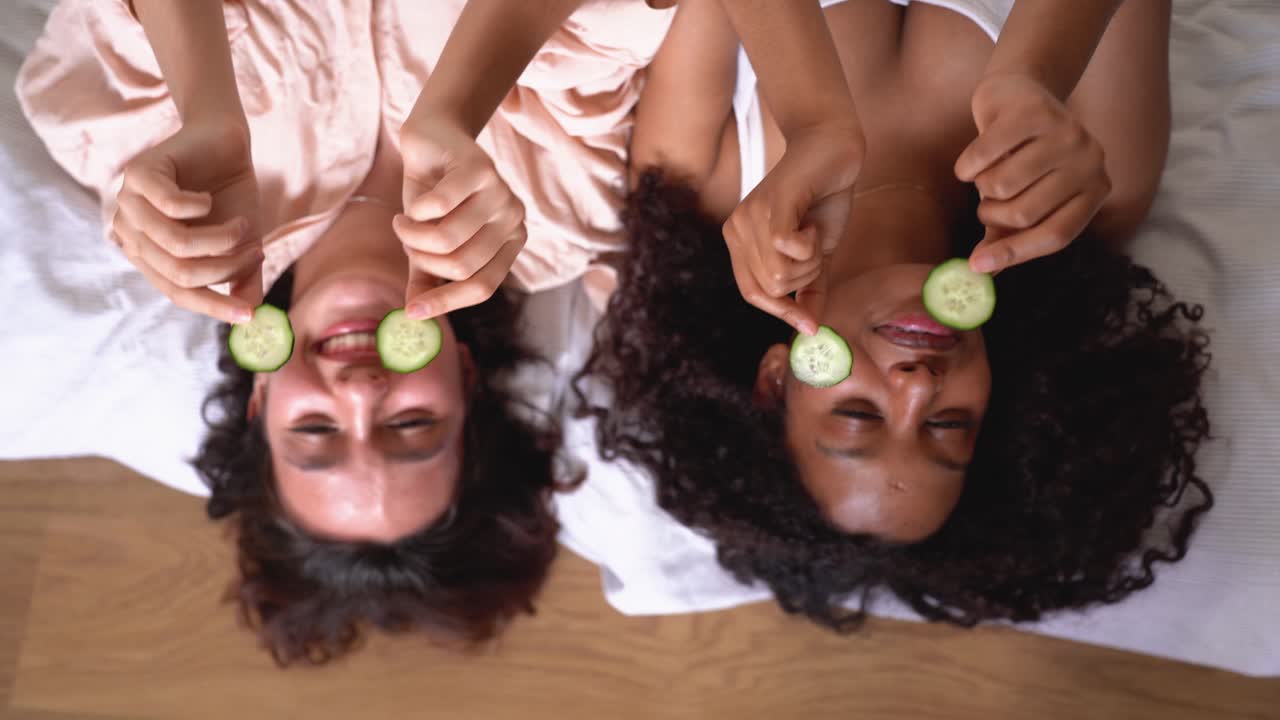 High angle of diverse women lying on blanket with cucumber slices on eyes