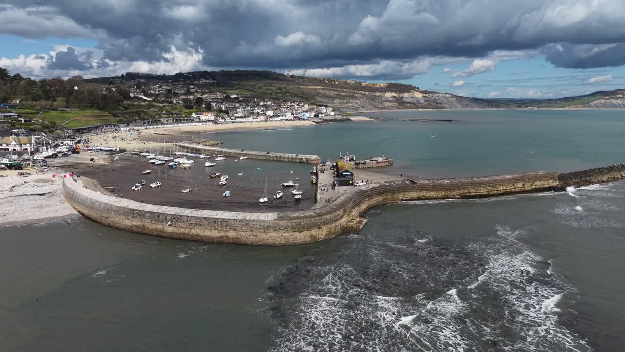 Vista aerea con drone del porto di Cobb a Lyme Regis, Devon, Regno Unito, con un cielo drammatico.