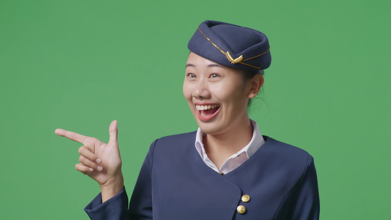 녹색 스크린 배경 스튜디오에 서 있는 동안 미소 짓고 을 가리키는 아시아 여성 에어 호스테이스의 클로즈업