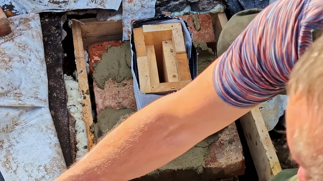 Mano che applica malta, costruendo una sezione della canna fumaria per la ristrutturazione, operaio che cementa muratura e casseforme, creando una struttura per camino, concentrandosi sulla riparazione del focolare