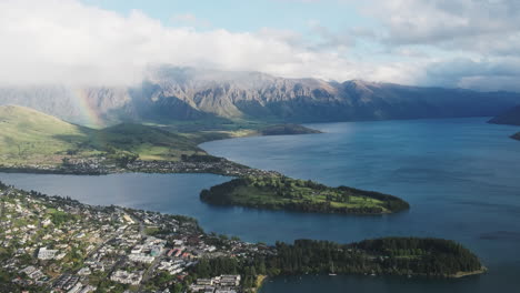 overlooking queenstown in new zealand, featuring a rainbow and scattered clouds, with blue sky visible