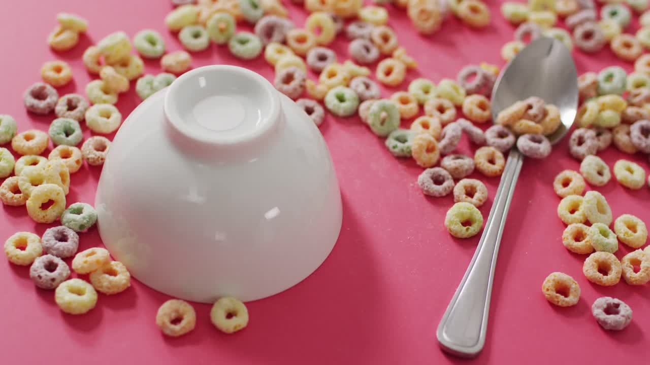 Video of colorful breakfast cereals with bowl and spoon on pink background