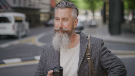 portrait of stylish businessman using smartphone checking messages waiting in city street holding coffee enjoying urban lifestyle slow motion