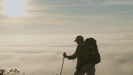 homem sênior escalando montanha com bastões de trekking ao pôr do sol