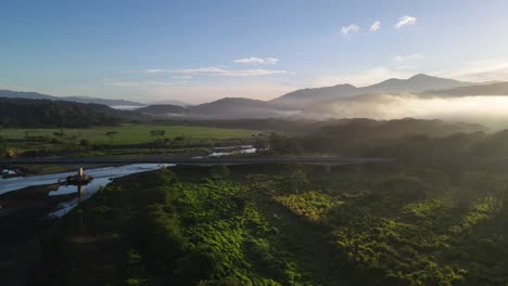 Imágenes-De-Drones-Del-Sol-Saliendo-Detrás-De-Una-Montaña-Con-Neblina-Matutina-Paralela-A-Un-Puente