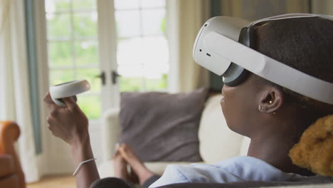 woman lying on sofa at home wearing vr headset with controllers and interacting with ar technology